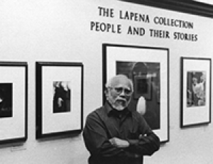 Photo of Frank LaPena standing in front of art gallery wall. 
